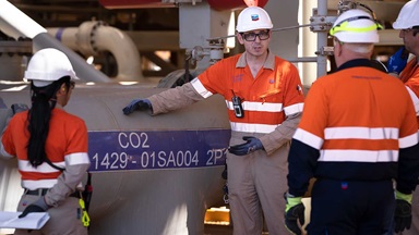 three workers look over a CO2 barrel and discuss ideas